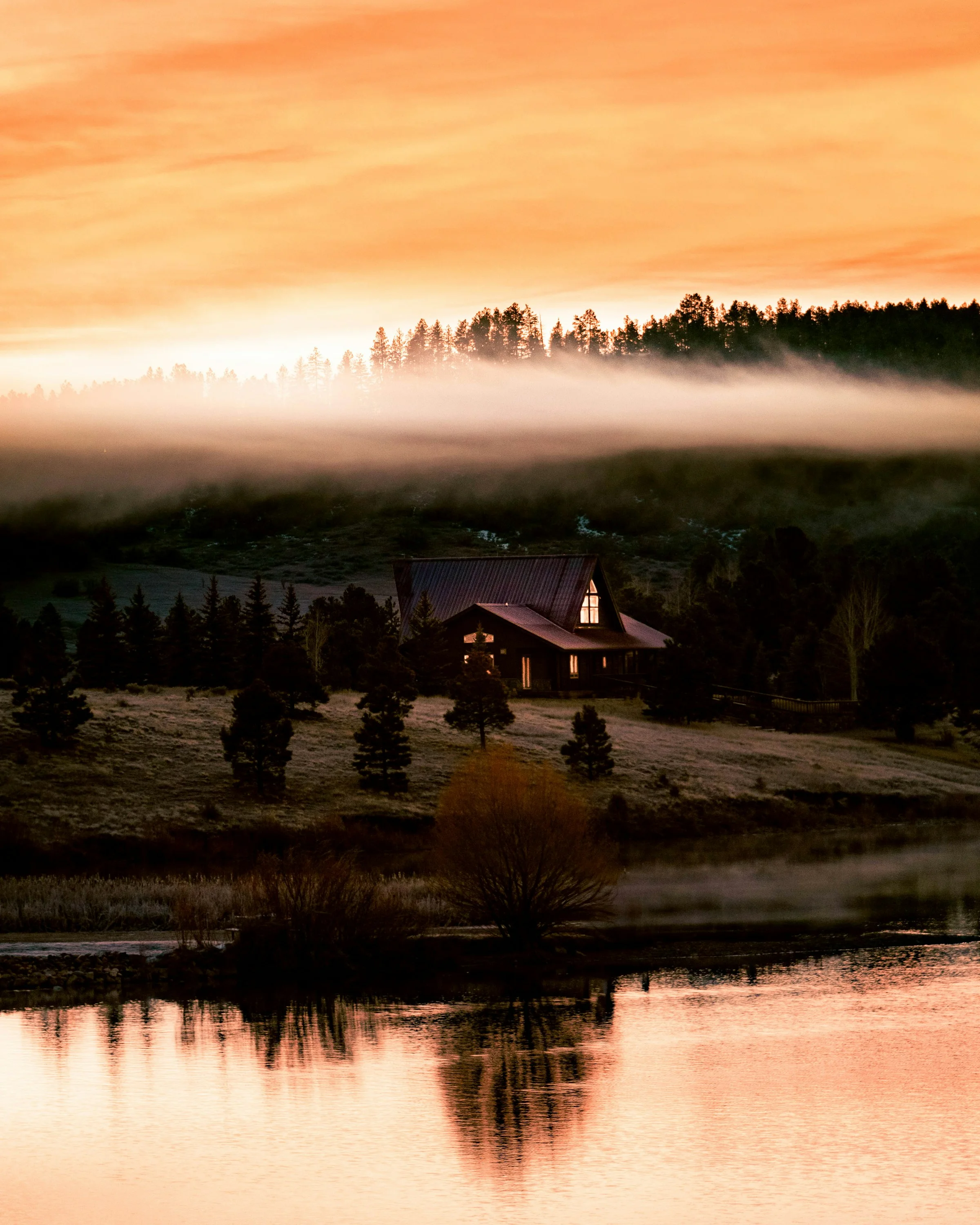 A timber lodge below a misty forest at sunrise
