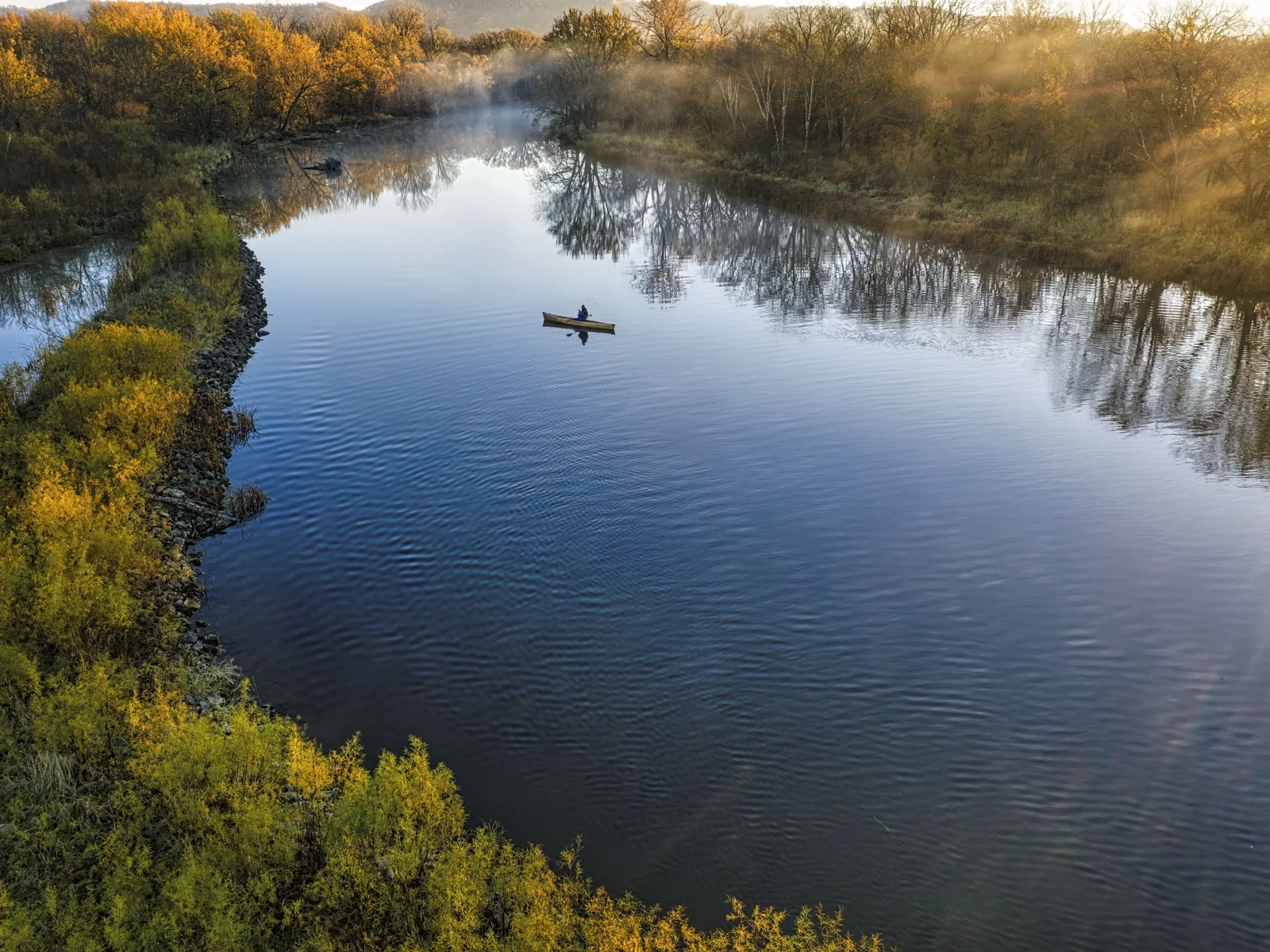 A lone kayaker paddling on a calm river at sunrise